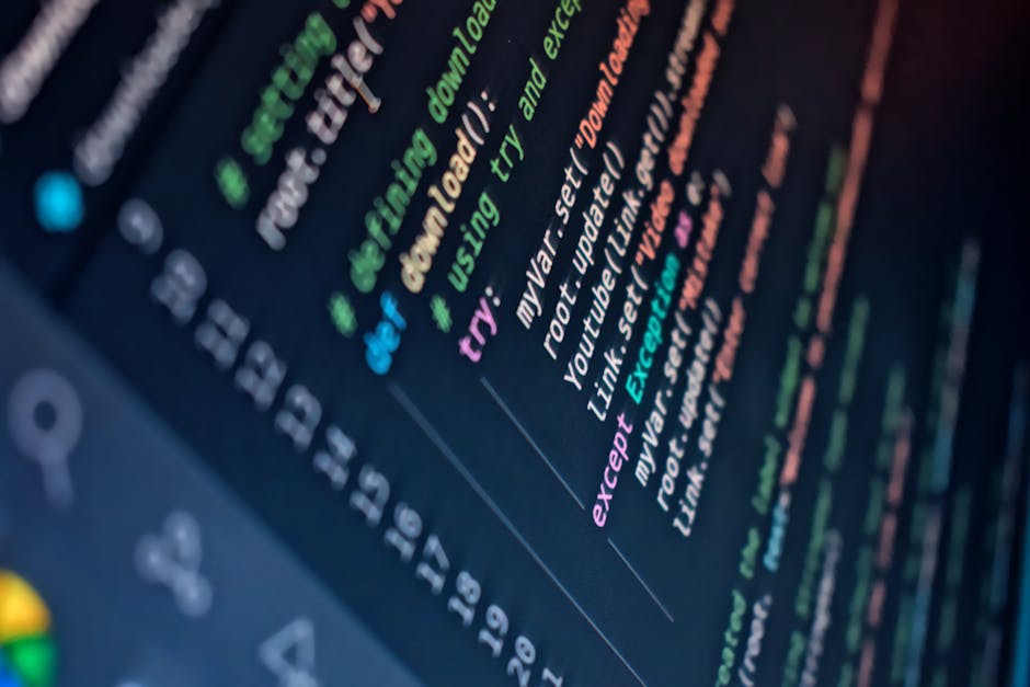 A close-up view of a computer screen displaying lines of colorful code, including green, pink, blue, and orange text on a dark background. The screen is tilted at an angle, with part of the keyboard v